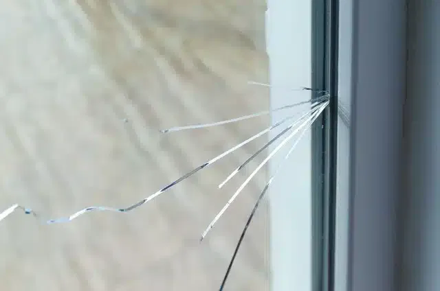 A damaged window with broken glass and a fractured frame, illustrating a state of disrepair and potential safety hazard.