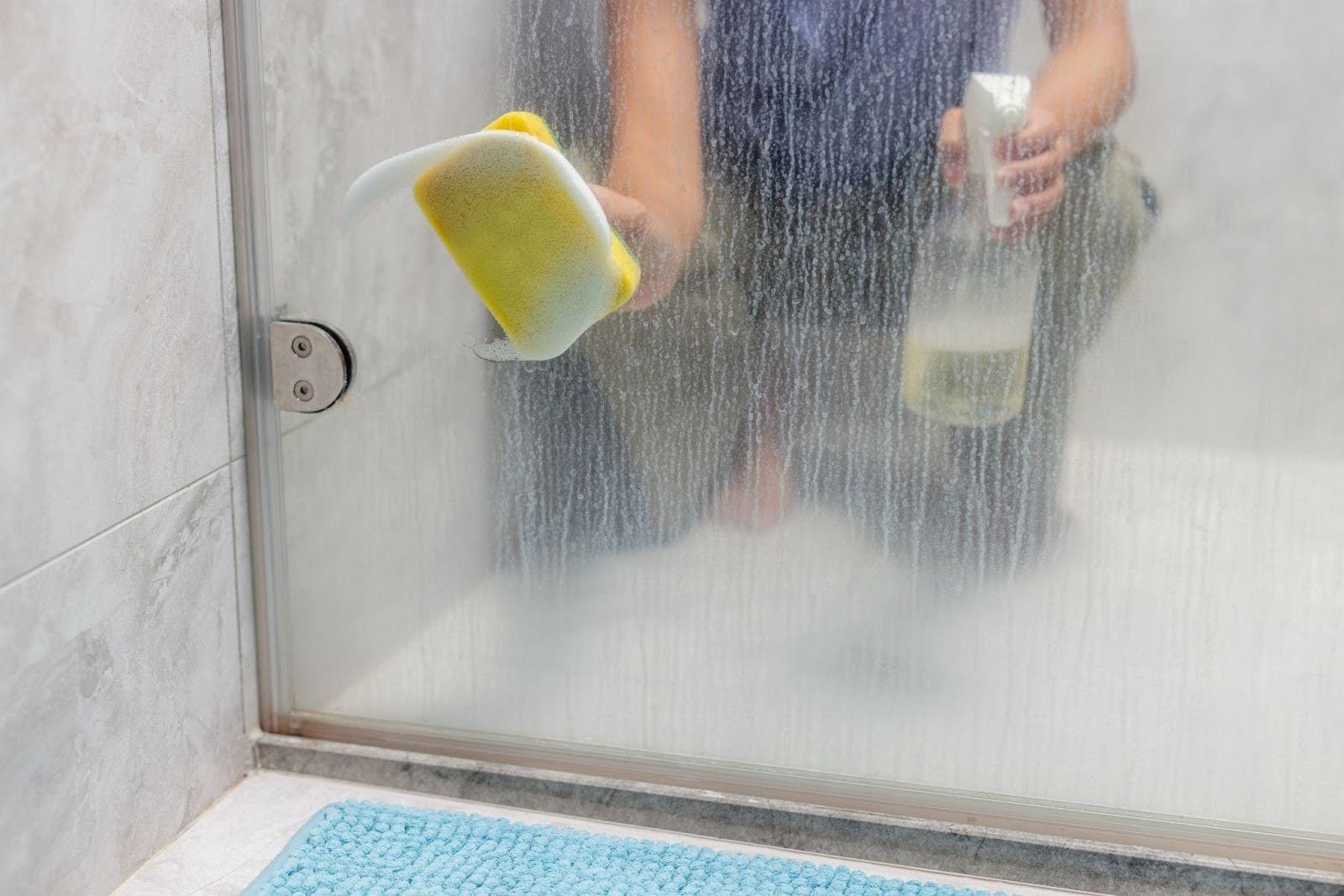 A person using a cloth to clean a glass shower door ensuring it is streak-free and shiny