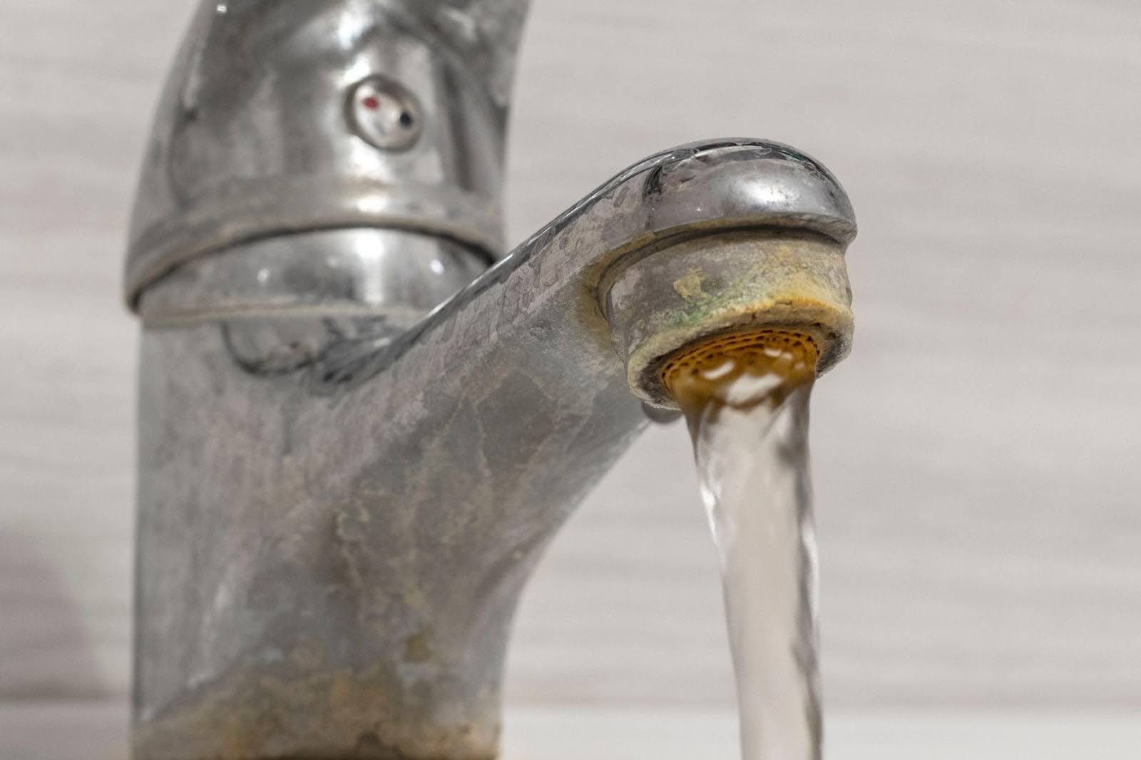Close-up of a faucet with a clear stream of water flowing against a blurred background