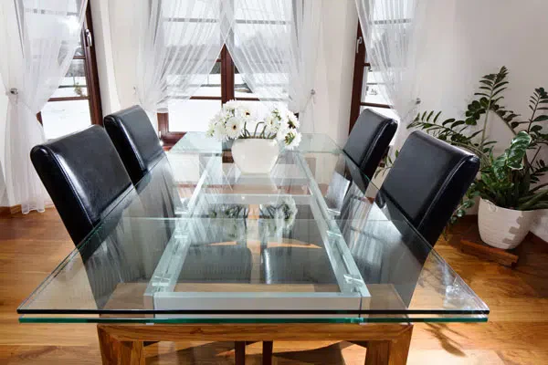 A glass dining table with four black chairs arranged around it.