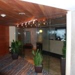 A lobby with glass walls, doors, and a plant in the middle.