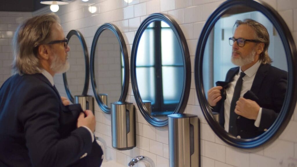 A man in a suit examines his reflection in three mirrors from different angles