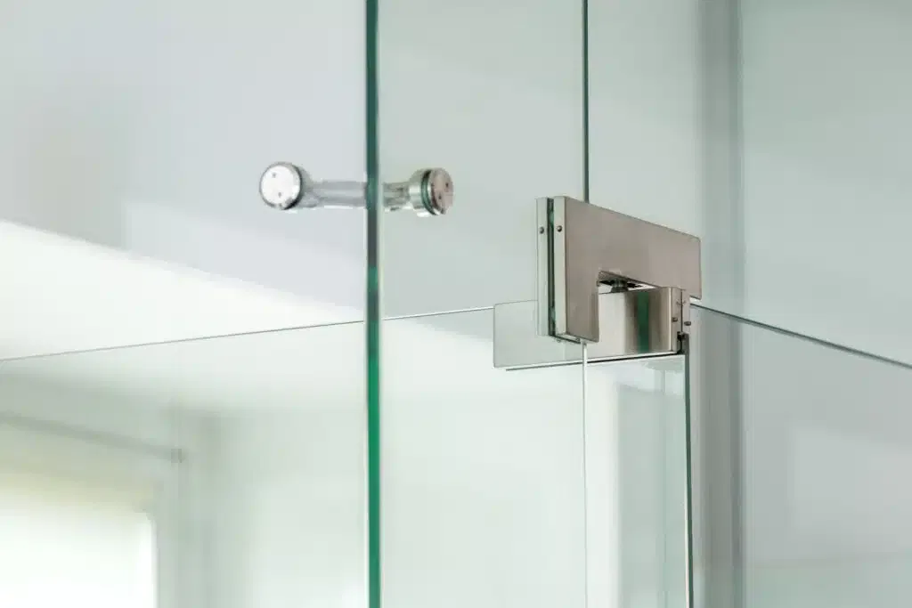 Close-up of a metal pivot hinge on a frameless glass shower door.