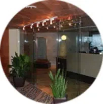 A lobby with glass walls, doors, and a plant in the middle.