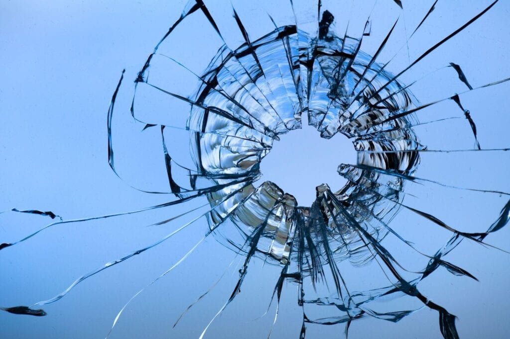 A broken window with a large hole and shattered fragments around the edges