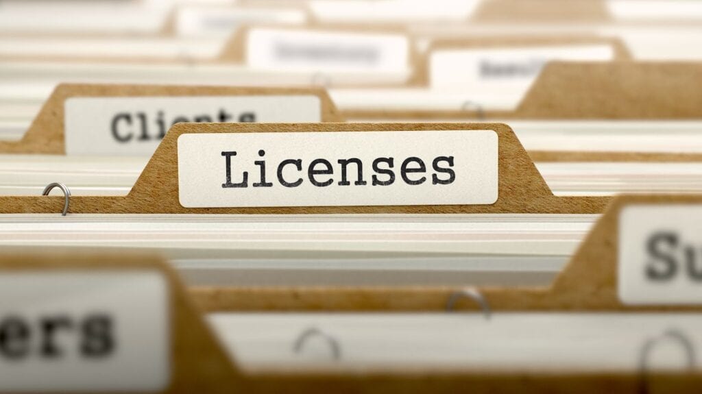 Various licenses and certificates neatly displayed on file folders in front of commercial glass doors.