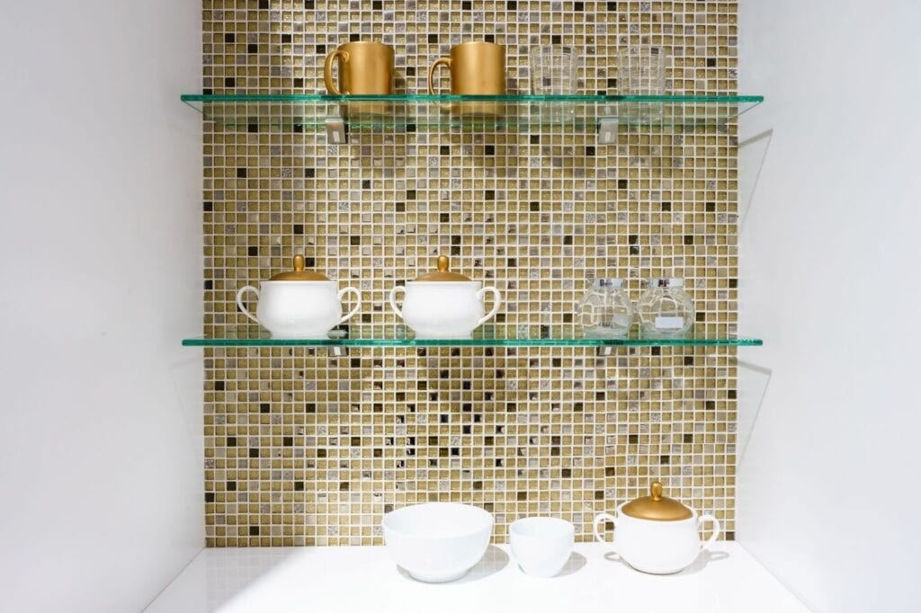 A glass shelf displaying elegant gold and white cups and saucers, showcasing a refined and stylish arrangement.