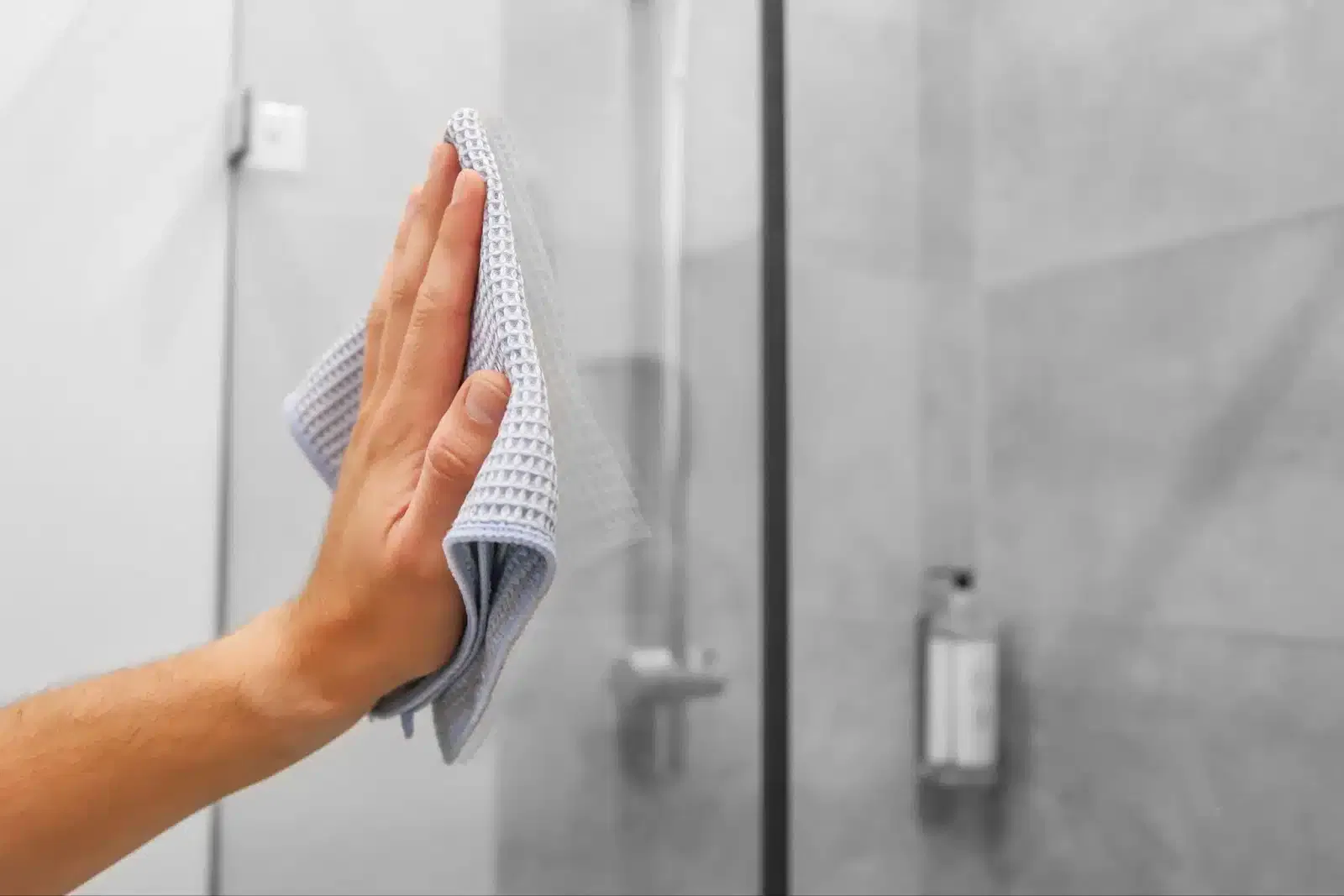 A person diligently cleans a glass shower door with a cloth, ensuring clarity and shine for optimal visibility.