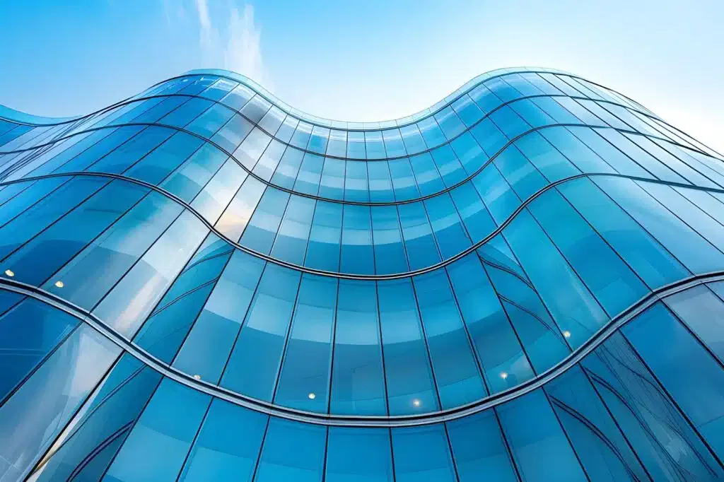 Modern glass building with a curved, wave-like facade reflecting the blue sky, creating a sleek and futuristic architectural design.