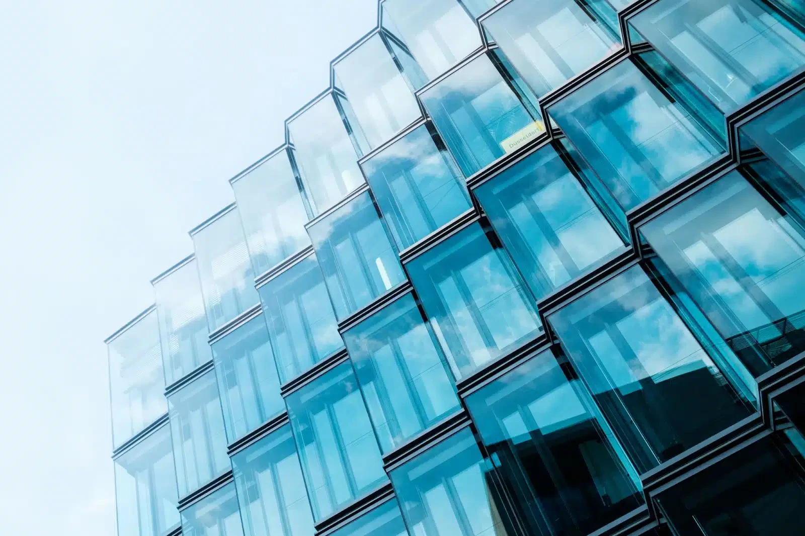 Modern glass building with a unique geometric facade reflecting the sky, showcasing contemporary architectural design.