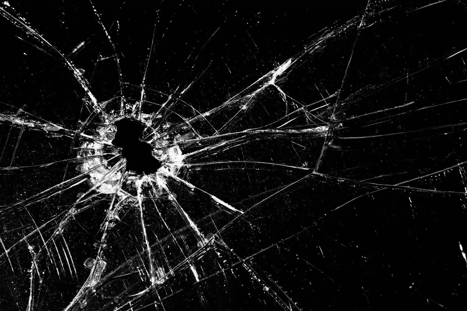 A broken window with a bullet hole in the center and shards scattered around