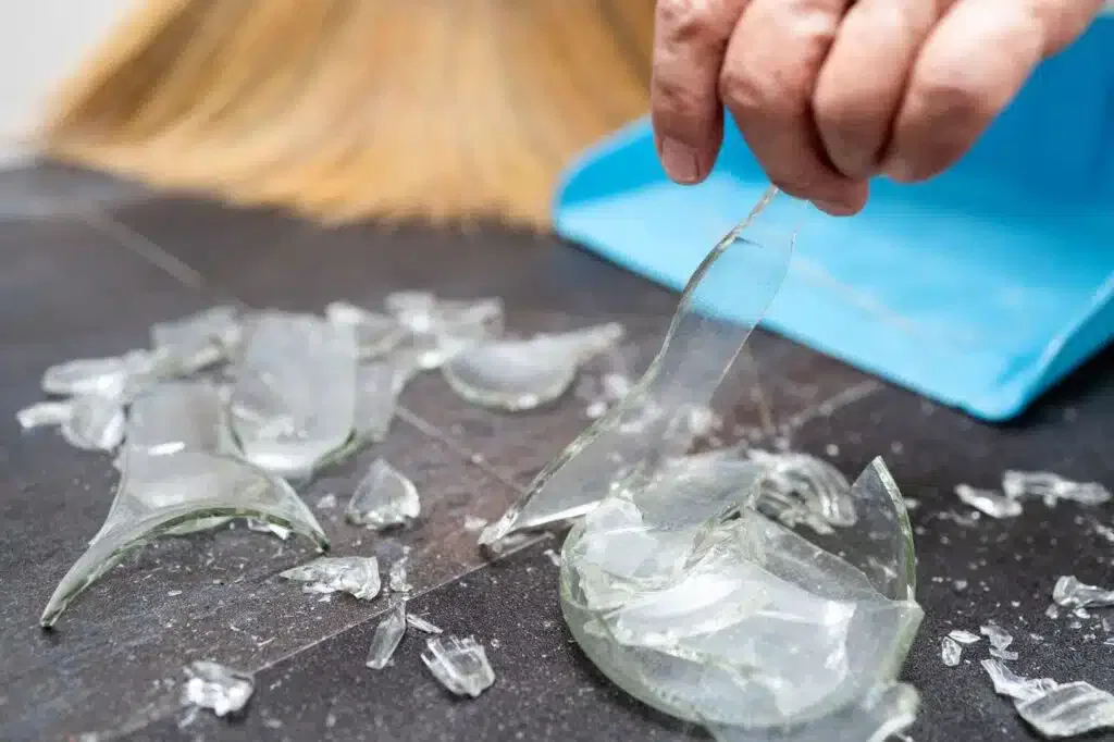 A person using a broom to clean up shards of broken glass on a floor
