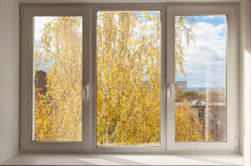 Window view of yellow autumn trees and a partly cloudy sky.