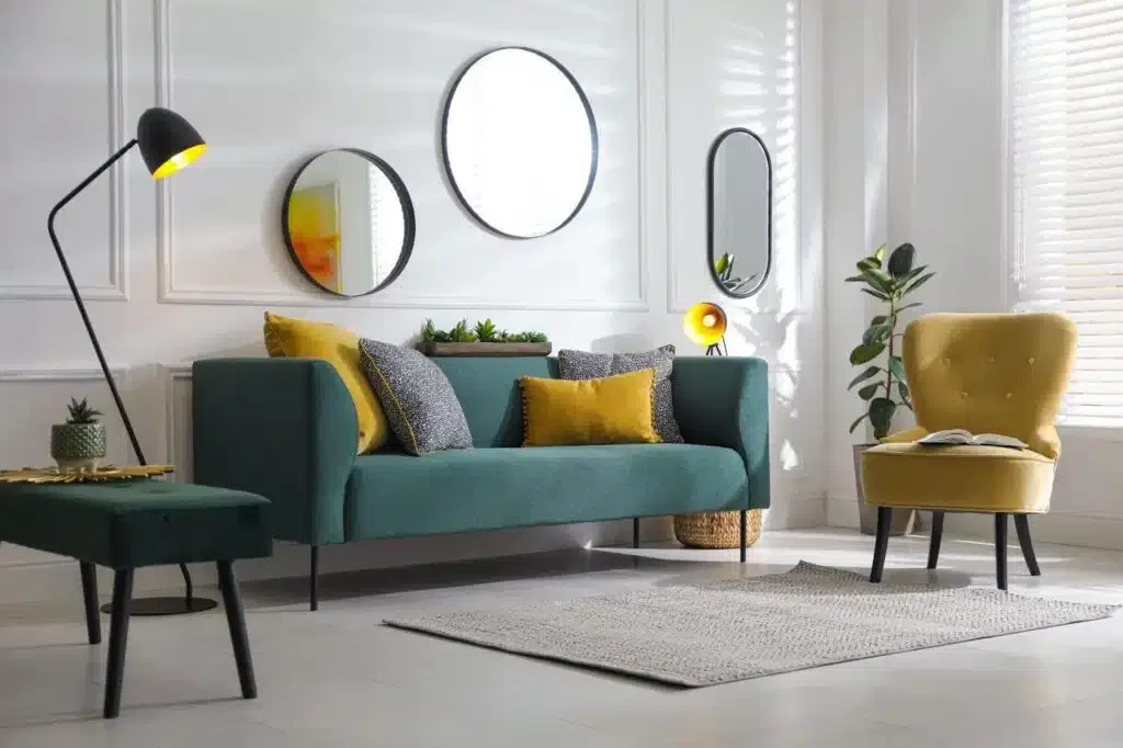 A living room featuring a green couch a yellow chair and a decorative mirror on the wall