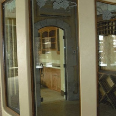 Circular window overlooking wine cellar with wooden barrels and hanging grapes.
