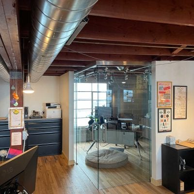 A glass-walled office with a cozy dog bed, providing a comfortable space for both work and relaxation.