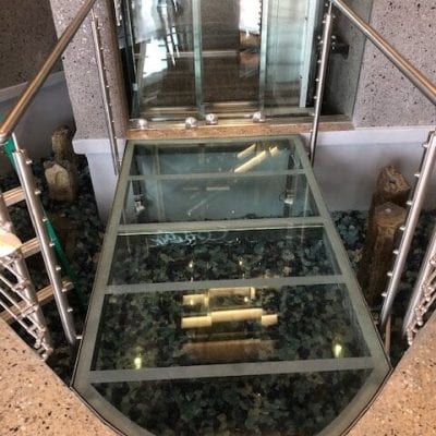 A glass elevator in a building with a transparent floor, offering a unique view of the surroundings.