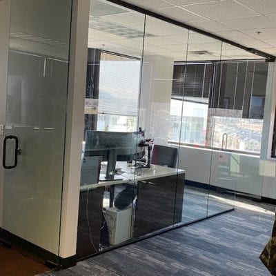 A modern glass-walled office with a desk and chair, providing a professional and open workspace.