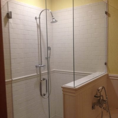A glass shower door with a shower head and a tub in a modern bathroom.